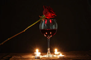 A delicate crimson red rose resting beside a gold-rimmed champagne glass on a white linen table.