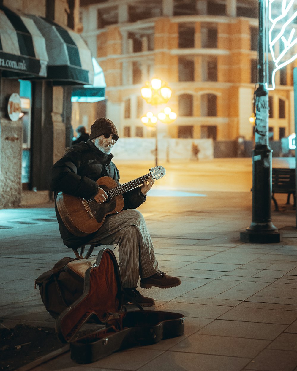 man playing guitar sitting on sidewalk during sunset