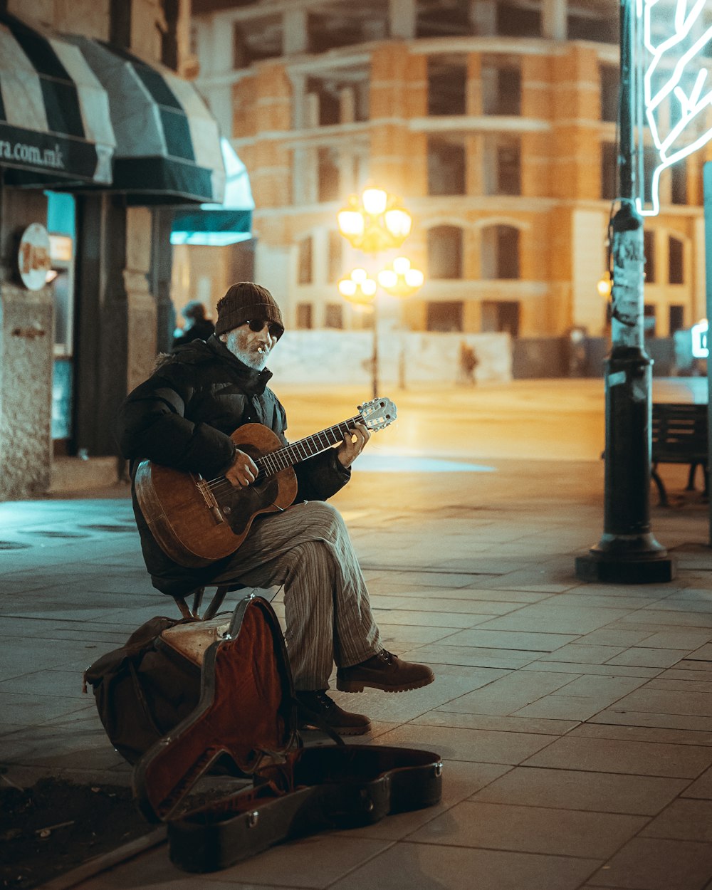 Mann spielt Gitarre und sitzt bei Sonnenuntergang auf dem Bürgersteig