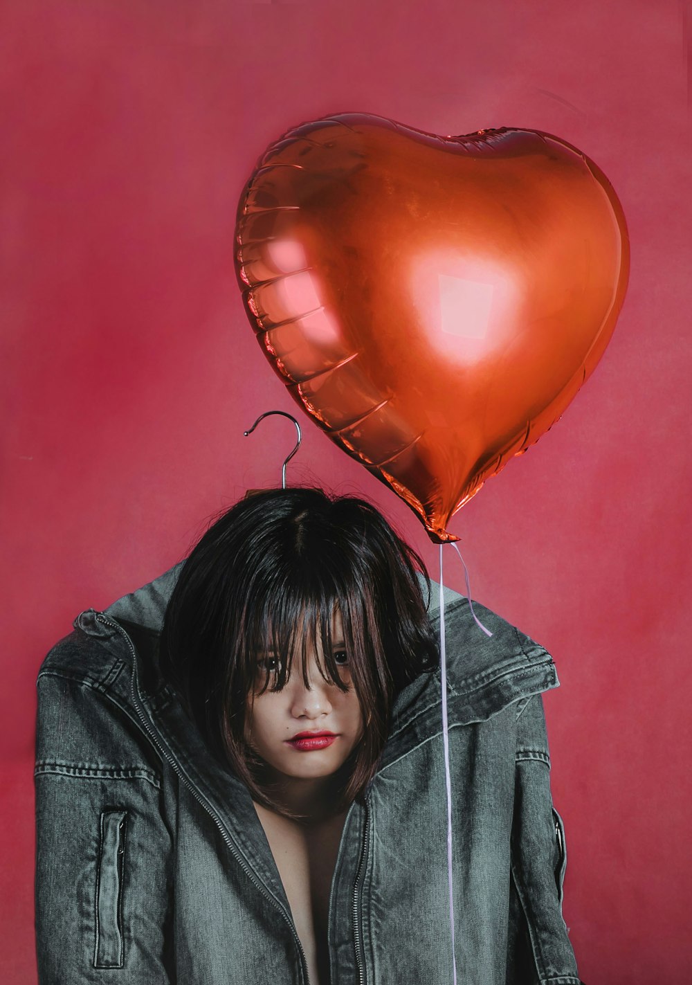 girl in gray jacket holding red balloon
