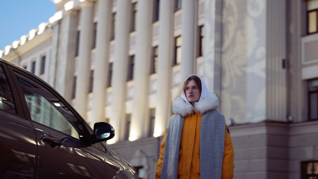 woman in brown and white coat standing beside black car during daytime