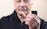 An older adult wearing a black jacket holds a set of dentures in their hand, with the focus on the dentures and the person's face slightly out of focus.
