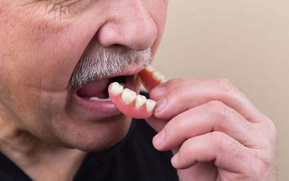 Technician carefully shaping a removable denture under focused lighting.