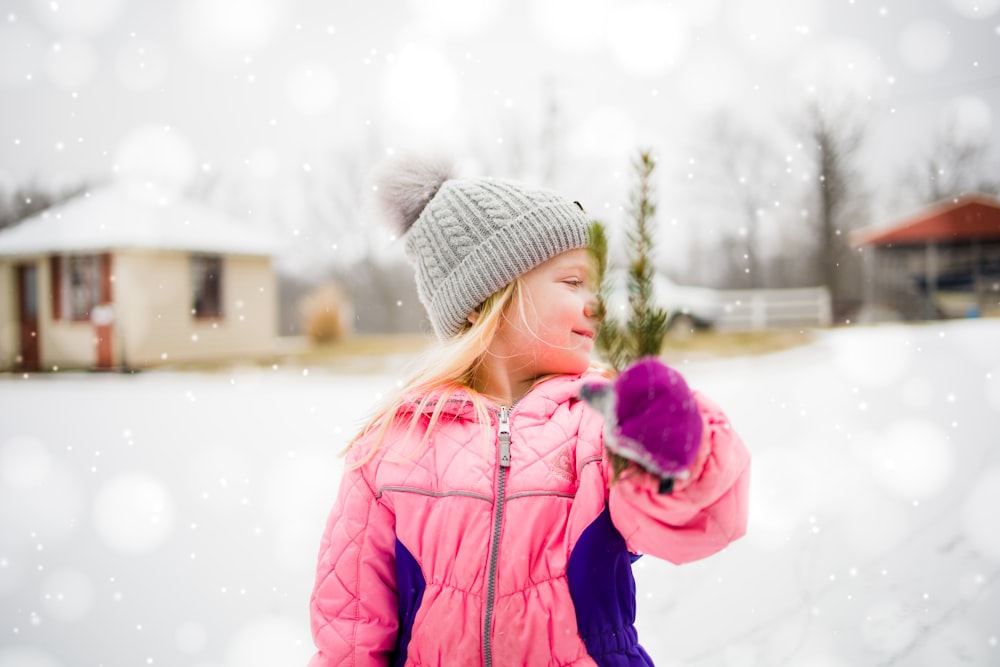 青いバブルジャケットとグレーのニット帽をかぶった女の子が、昼間、雪に覆われた地面に立っています