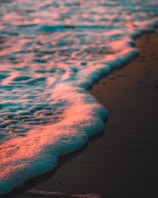 Gentle waves lapping on a sandy shore tinted with warm soft orange hues.