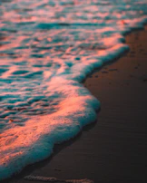 Gentle waves lapping on a sandy beach under a soft pink and beige sunset sky, evoking peace and renewal.