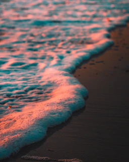 Gentle waves lapping on a sandy beach under a soft pink and beige sunset sky, evoking peace and renewal.