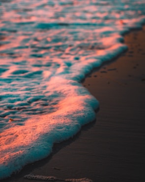 Gentle waves lapping on a sandy shore tinted with warm soft orange hues.