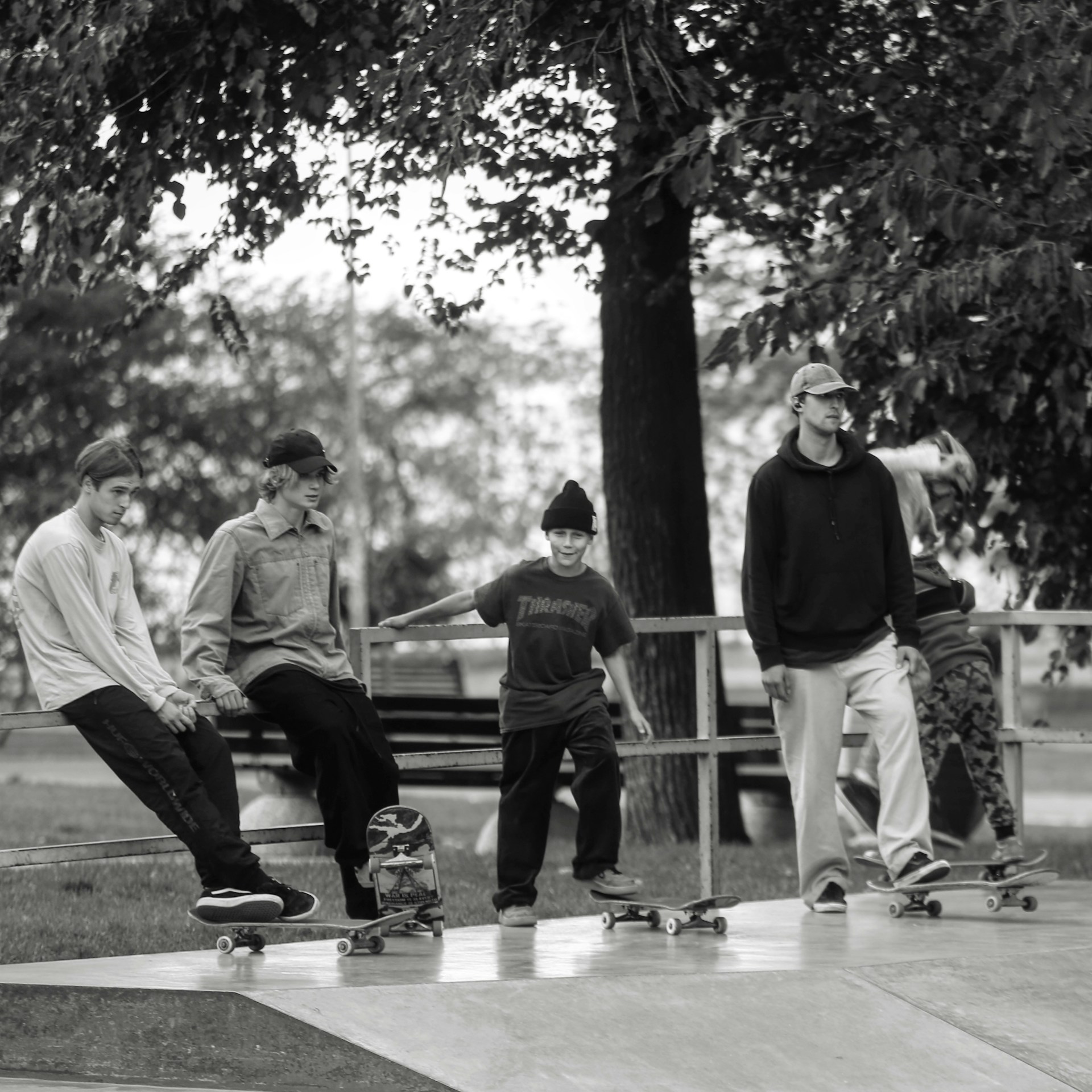 A group of friends hanging out by a skatepark, dressed in a mix of black and white baggy clothes, laughing and showing off their style.