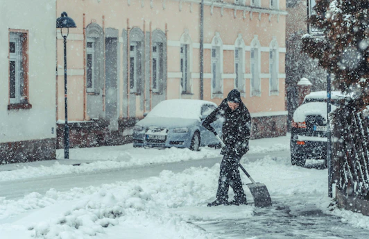 person in black jacket and pants holding snow shovel on snow covered ground during daytime