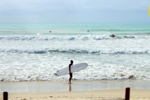 man in black wet suit holding white surfboard walking on beach during daytime
