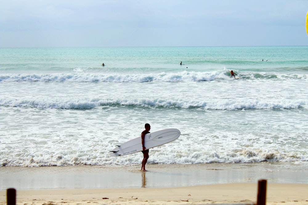 man in black wet suit holding white surfboard walking on beach during daytime