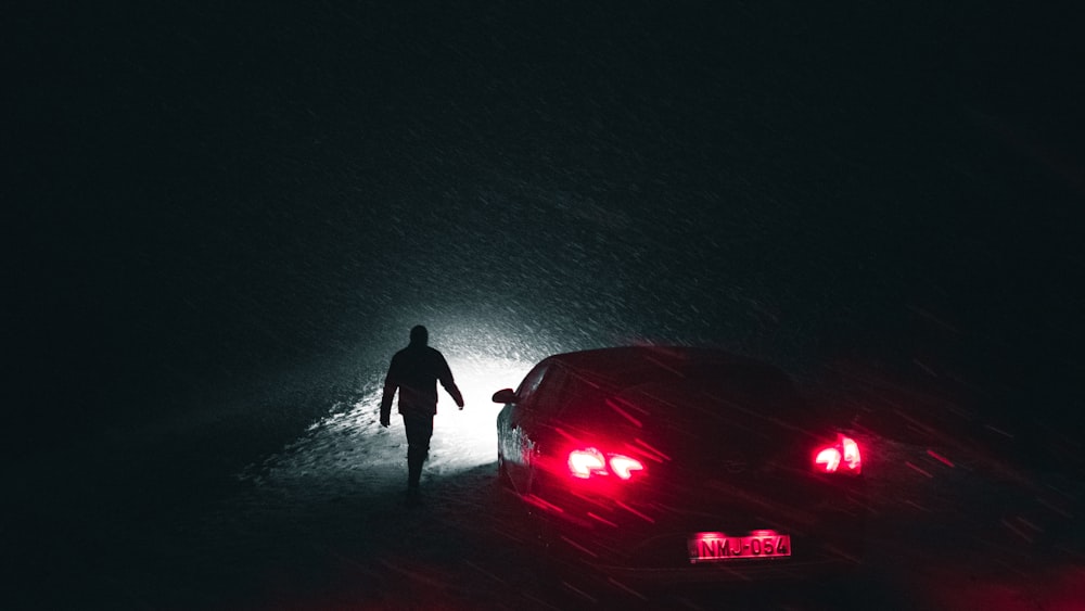 man in black jacket standing beside red car during nighttime