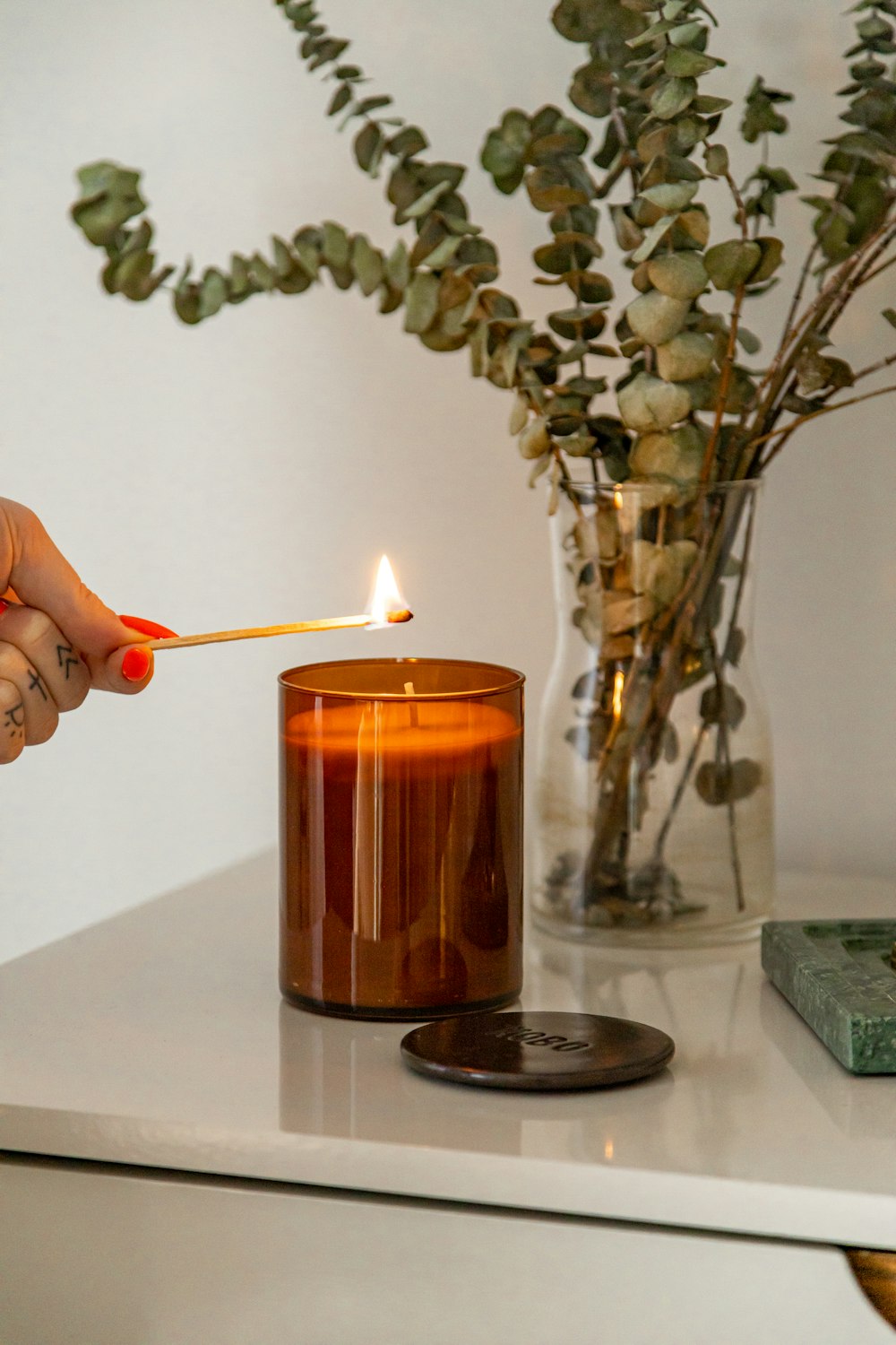 person holding lighted candle near green plant