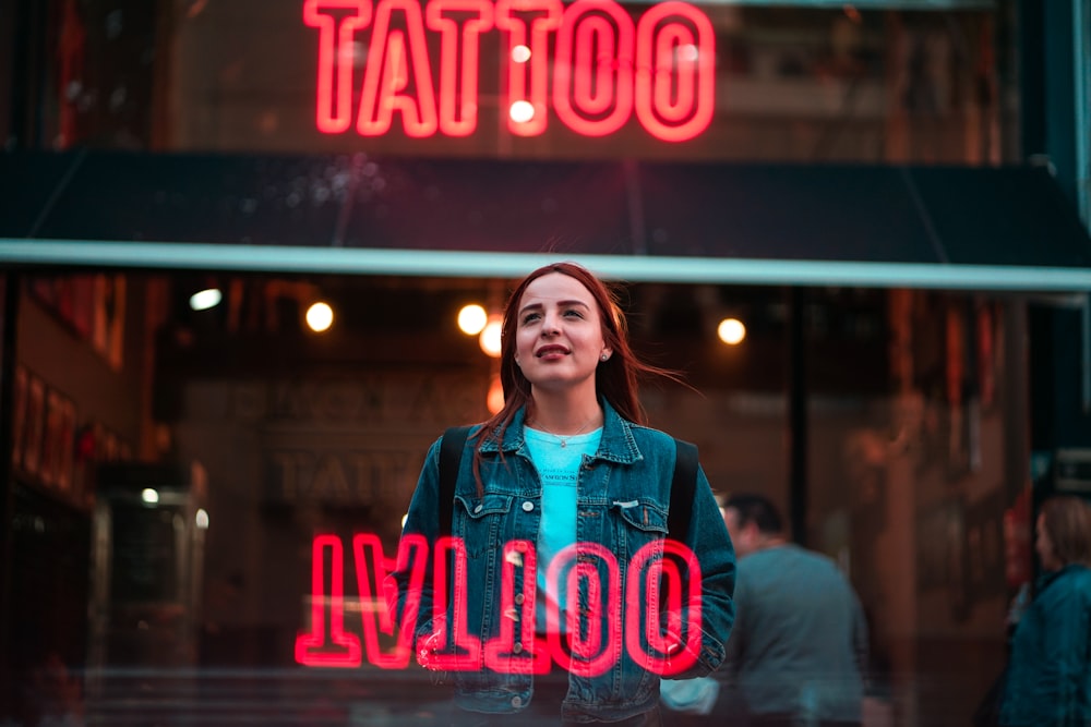 woman in blue zip up jacket standing in front of red and blue open neon signage