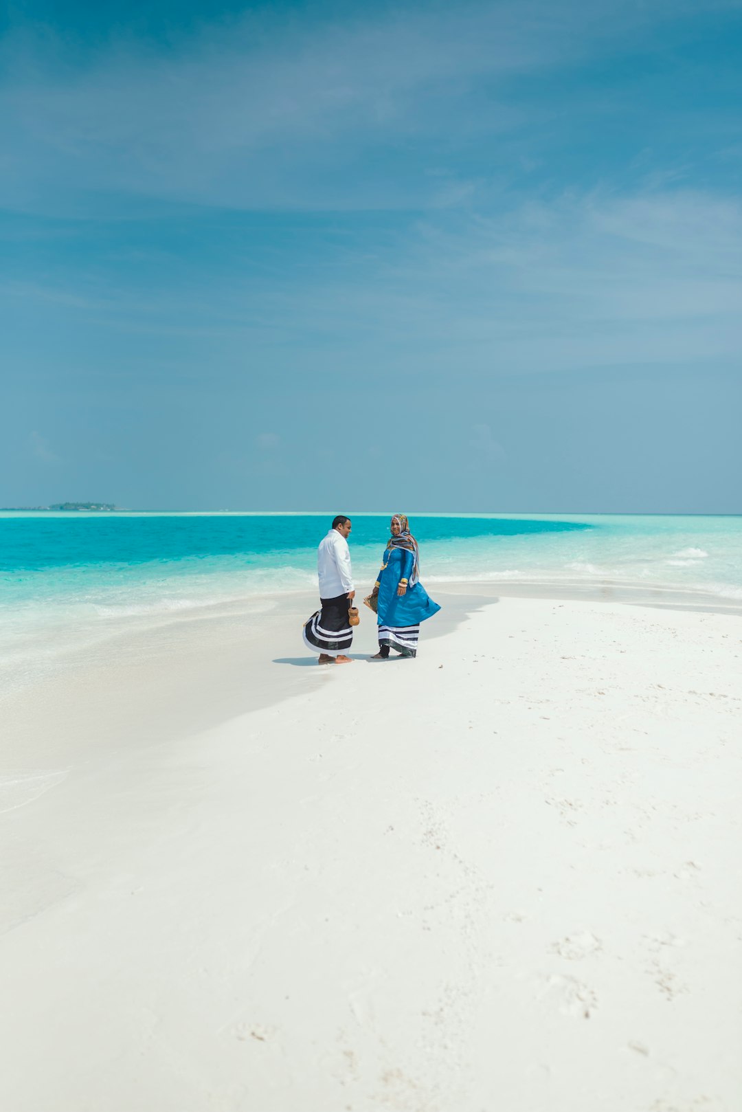 couple sitting on white sand beach during daytime