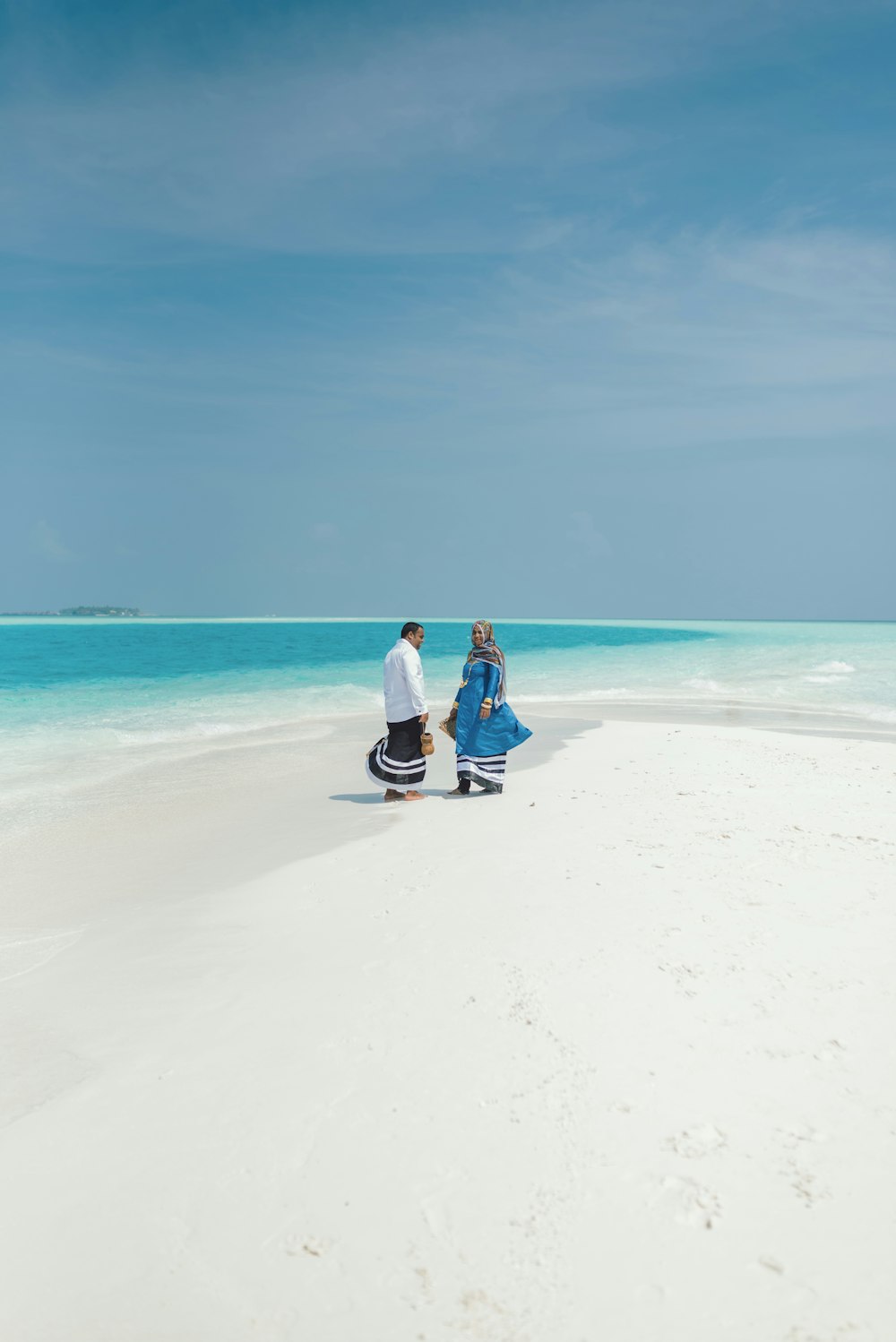 couple sitting on white sand beach during daytime