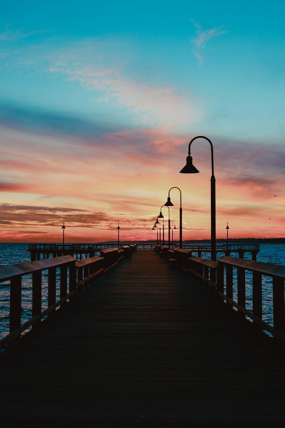 silhouette of person walking on wooden dock during sunset