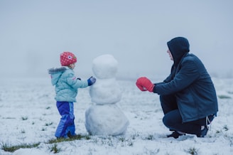 man in black jacket and blue pants sitting on white snow covered ground