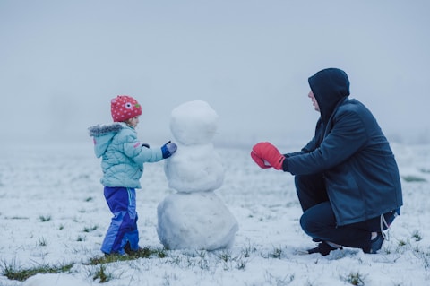 man in black jacket and blue pants sitting on white snow covered ground
