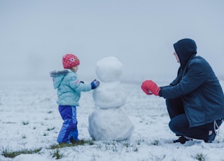 man in black jacket and blue pants sitting on white snow covered ground