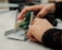 Hands are manipulating a small mechanical assembly, which includes metal and plastic components. The setup seems to involve green gears and metallic rods, indicative of a robotics or engineering-related activity.
