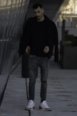 Model walking through an urban alley wearing layered black streetwear with subtle reflective accents.