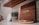 A wooden sign with the word 'ALOHA' sits on a kitchen counter. Next to the sign is a plant in a patterned pot. A wooden shelf hangs above with a small white marble cutting board leaning against the backsplash. Below, a soap dish holds a bar of soap.