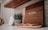 A wooden sign with the word 'ALOHA' sits on a kitchen counter. Next to the sign is a plant in a patterned pot. A wooden shelf hangs above with a small white marble cutting board leaning against the backsplash. Below, a soap dish holds a bar of soap.