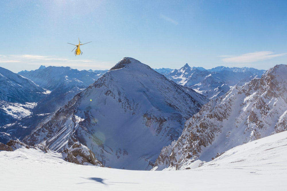 yellow and black helicopter flying over snow covered mountain during daytime