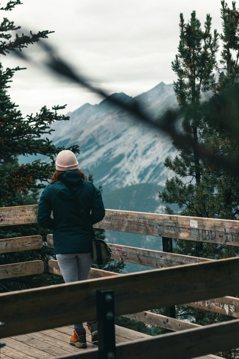 person in black jacket and white cap standing on brown wooden bridge during daytime