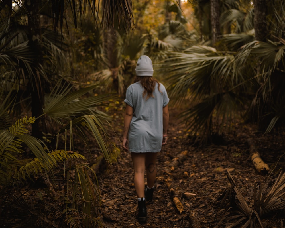 woman in white dress shirt and white hat standing in the middle of the forest during