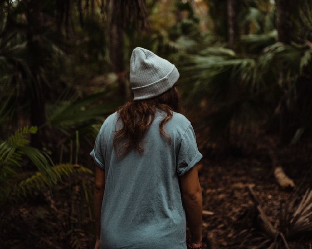 Donna in maglietta blu e cappello bianco in piedi nel bosco