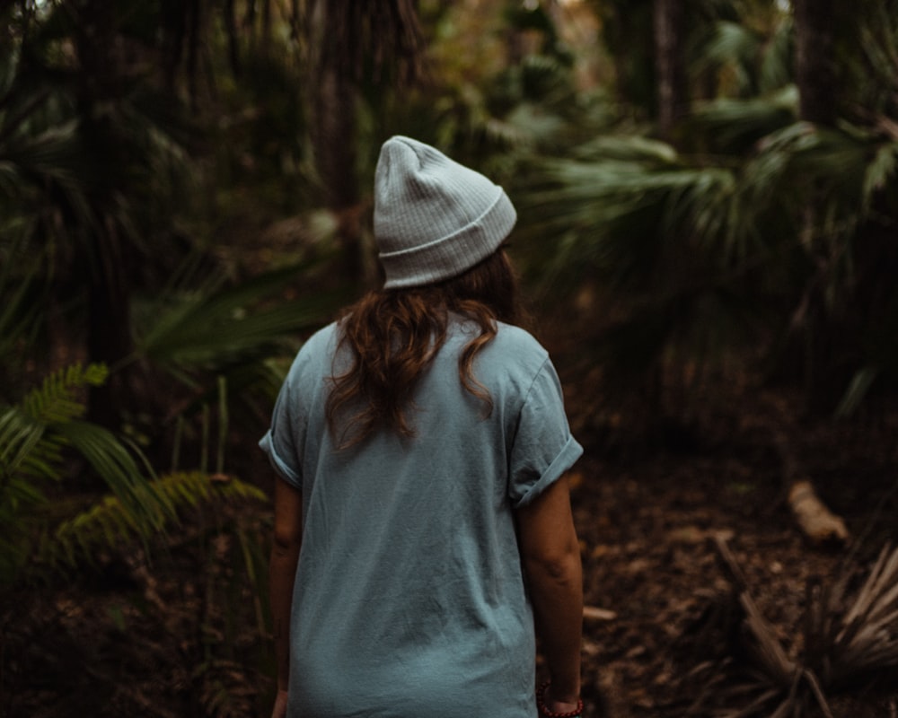 woman in blue t-shirt and white hat standing in the woods