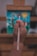 A child's hand is holding a paintbrush against a colorful canvas on an easel. The painting features abstract shapes and bright colors, including a sun-like figure. The focus is on the child's hand, emphasizing the act of painting.