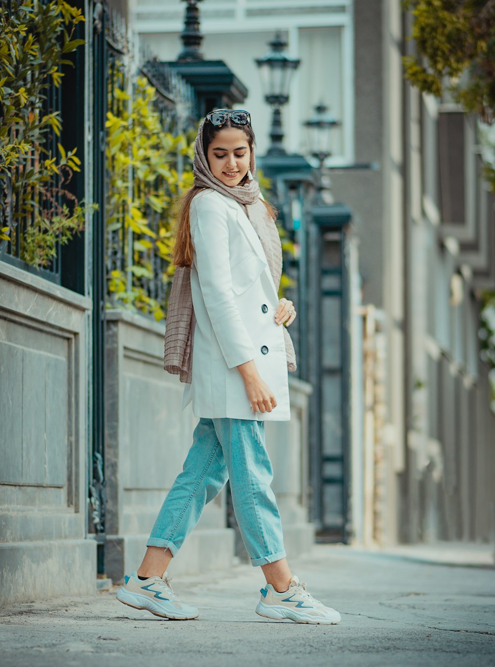 woman in white coat and blue denim jeans standing near white concrete building during daytime