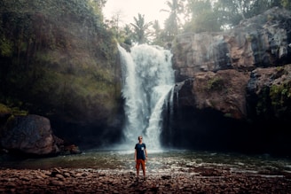 man in orange shirt standing near waterfalls during daytime in bali