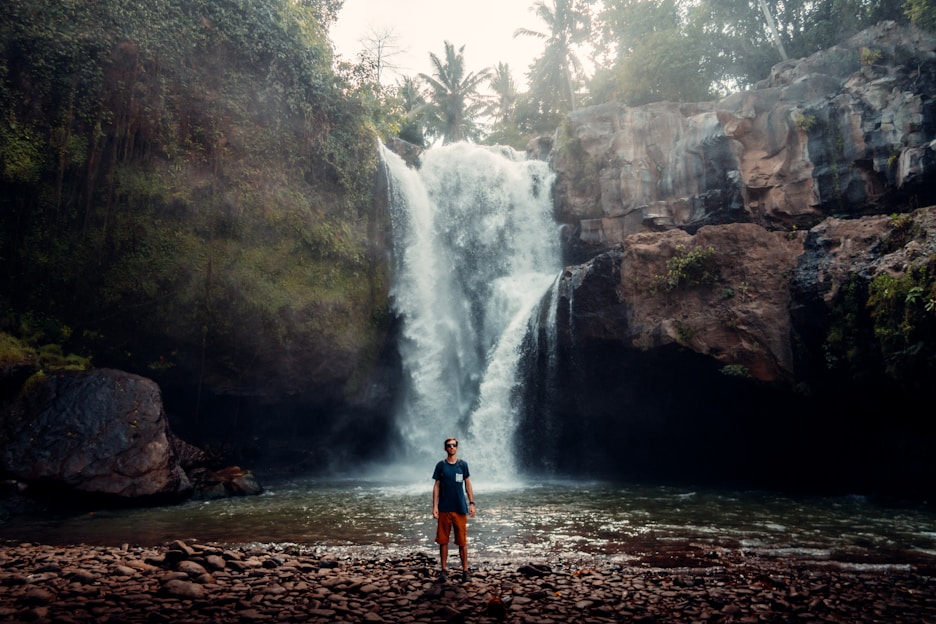 man in orange shirt standing near waterfalls during daytime in bali