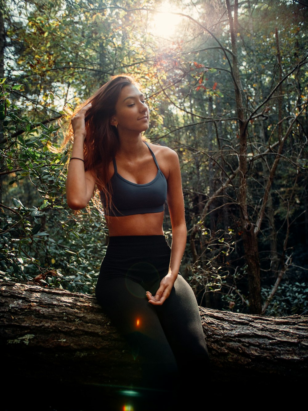woman in blue sports bra and black leggings sitting on tree log during daytime