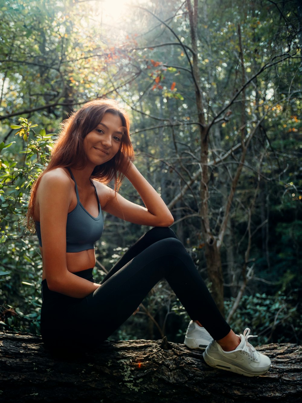 donna in reggiseno sportivo bianco e pantaloni neri in piedi sul tronco d'albero durante il giorno