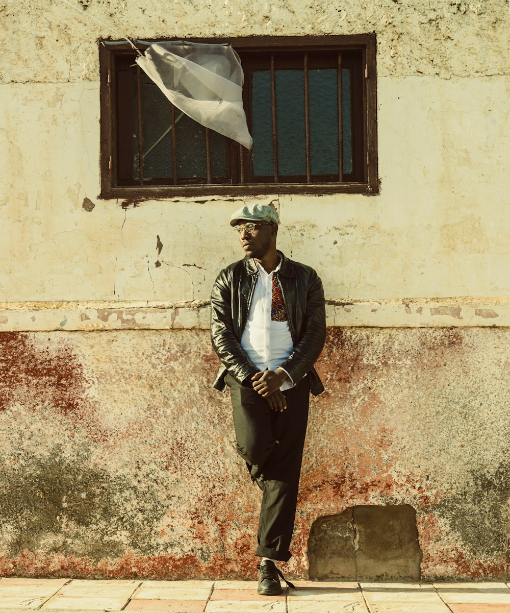 man in blue dress shirt and brown pants standing beside white concrete wall during daytime