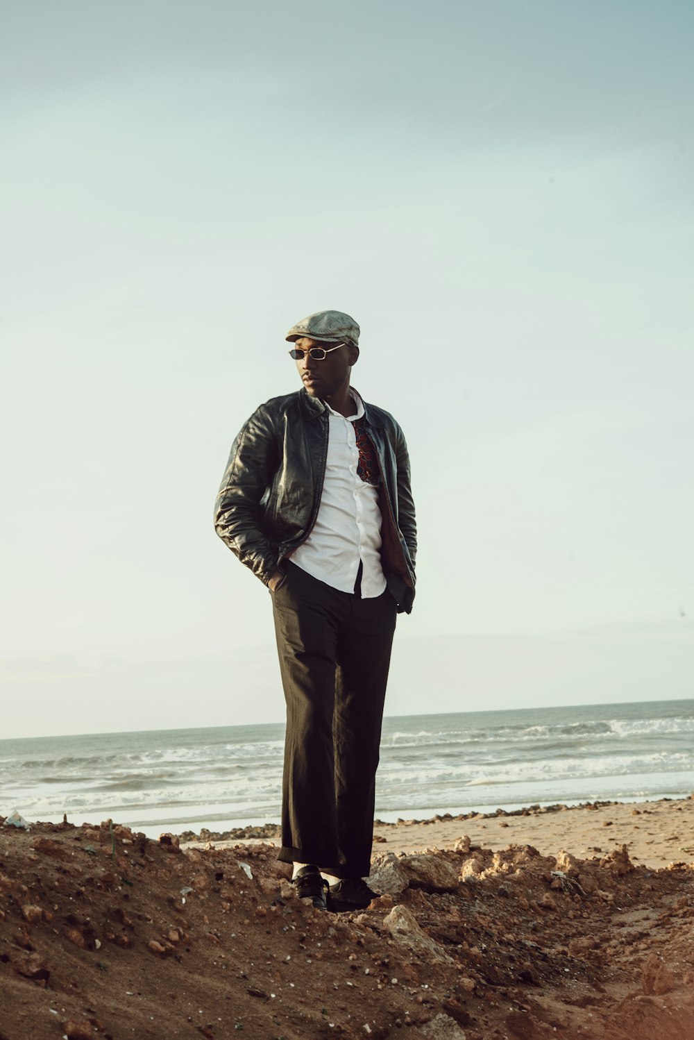 man in black leather jacket standing on brown sand near sea during daytime