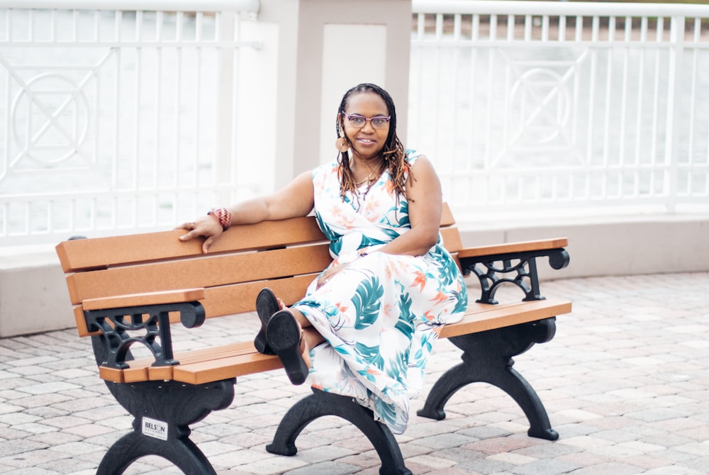 woman in white and blue floral dress sitting on brown wooden bench