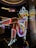 A brightly lit neon sign of a cowgirl wearing a white hat, boots, and a red, white, and blue outfit. The figure is sitting with one leg raised and crossed, in a lively and colorful style, suggestive of a vintage or retro aesthetic.