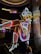 A brightly lit neon sign of a cowgirl wearing a white hat, boots, and a red, white, and blue outfit. The figure is sitting with one leg raised and crossed, in a lively and colorful style, suggestive of a vintage or retro aesthetic.