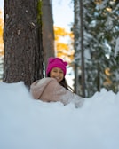 woman in pink knit cap and white knit scarf sitting on snow covered ground near brown