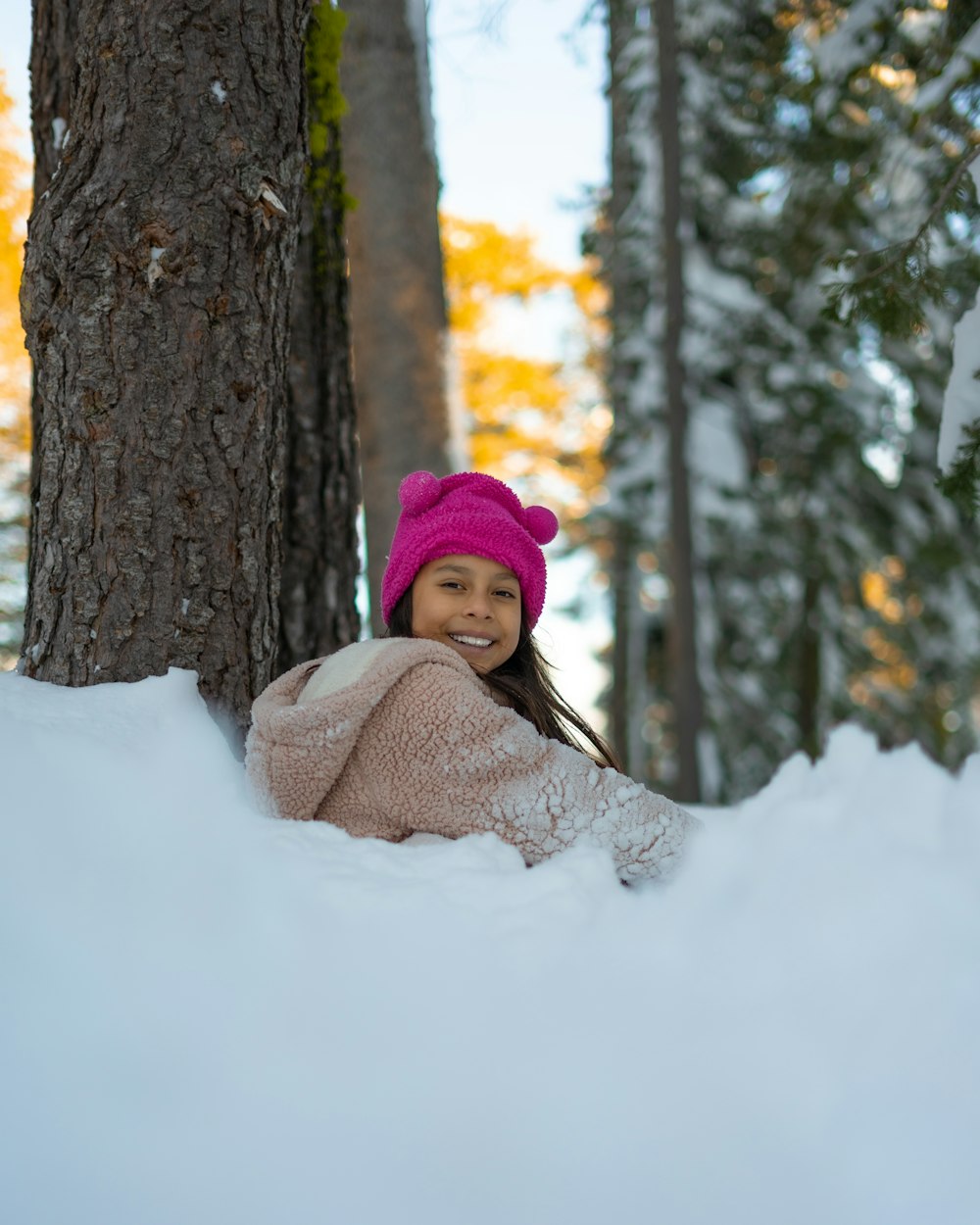 woman in pink knit cap and white knit scarf sitting on snow covered ground near brown