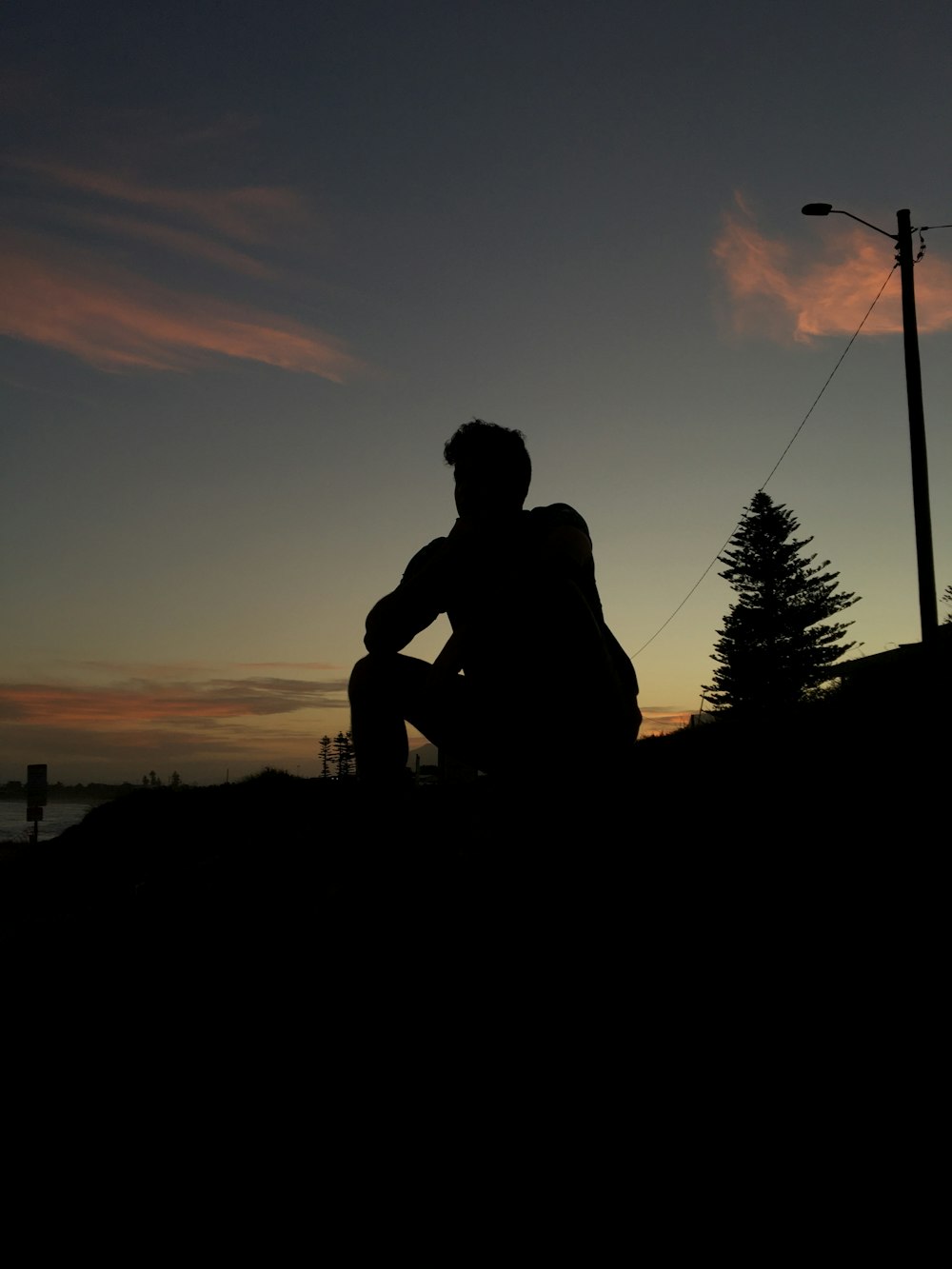 Silueta del hombre sentado en la roca durante la puesta del sol