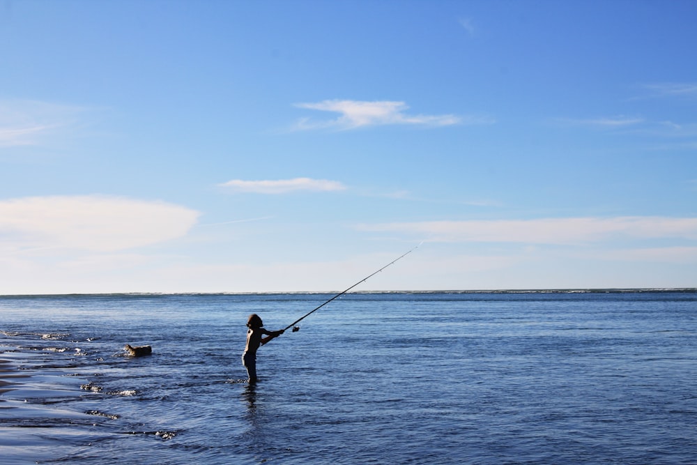 Mujer en bikini negro sosteniendo caña de pescar en el mar durante el día