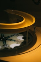 A close-up view of a vintage pinball machine component with a yellow curved feature and a visible playfield marked with numbers and the word 'BINGO'. The machine has a retro design with some metal elements.